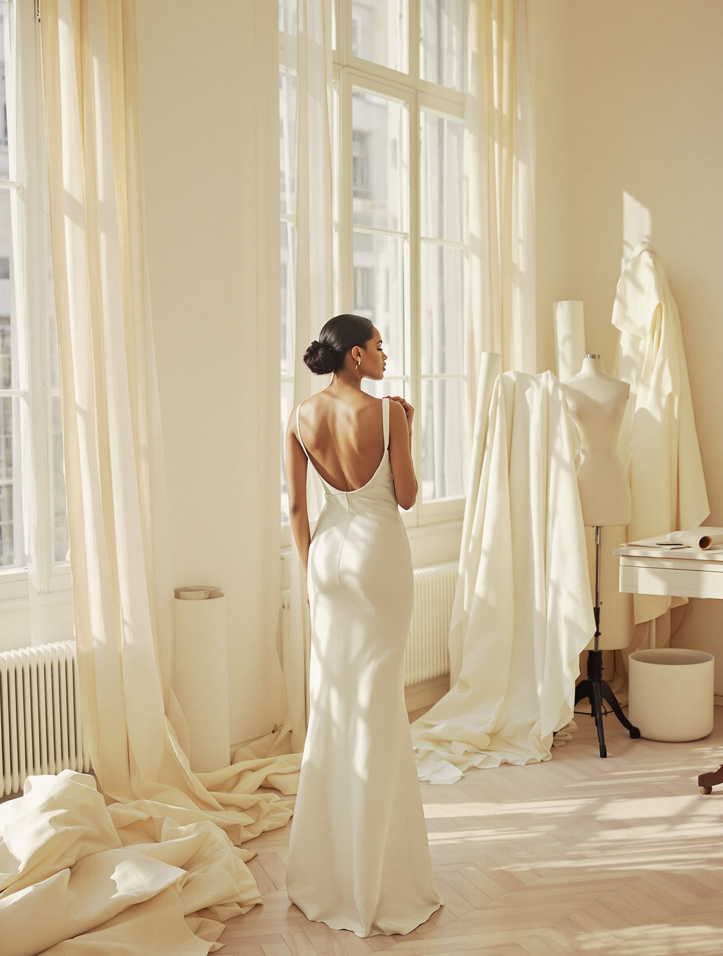 From behind, in an ivory dress, in a sunlit Parisian atelier